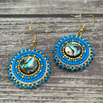 Handmade drop earrings with abalone shell button, seed beads, 24kt gold beads, hide backing, and 18kt gold hooks, 2” long.