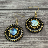 Handmade drop earrings with abalone shell button, seed beads, 24kt gold beads, hide backing, and 18kt gold hooks, 2” long.
