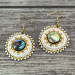 Handmade drop earrings with abalone shell button, seed beads, 24kt gold beads, hide backing, and 18kt gold hooks, 2” long.