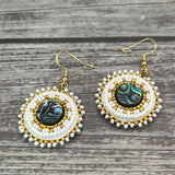 Handmade drop earrings with abalone shell button, seed beads, 24kt gold beads, hide backing, and 18kt gold hooks, 2” long.