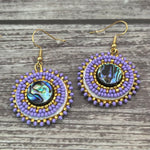 Handmade drop earrings with abalone shell button, seed beads, 24kt gold beads, hide backing, and 18kt gold hooks, 2” long.