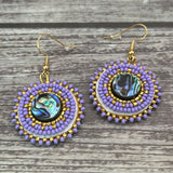 Handmade drop earrings with abalone shell button, seed beads, 24kt gold beads, hide backing, and 18kt gold hooks, 2” long.