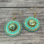 Handmade drop earrings with abalone shell button, seed beads, 24kt gold beads, hide backing, and 18kt gold hooks, 2” long.