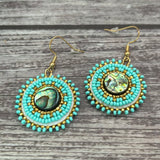 Handmade drop earrings with abalone shell button, seed beads, 24kt gold beads, hide backing, and 18kt gold hooks, 2” long.