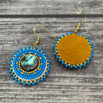 Handmade drop earrings with abalone shell button, seed beads, 24kt gold beads, hide backing, and 18kt gold hooks, 2” long.