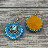 Handmade drop earrings with abalone shell button, seed beads, 24kt gold beads, hide backing, and 18kt gold hooks, 2” long.