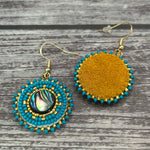 Handmade drop earrings with abalone shell button, seed beads, 24kt gold beads, hide backing, and 18kt gold hooks, 2” long.